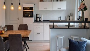 A modern kitchen with white cabinetry, a wooden dining table, and bar stools. - Schwedengang 7A Whg.1 Unten Links (Zingst)