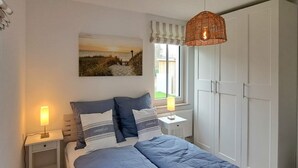 A bedroom with a bed, two bedside tables, a hanging light fixture, a window with curtains, and a wardrobe. - Schwedengang 7A Whg.1 Unten Links (Zingst)