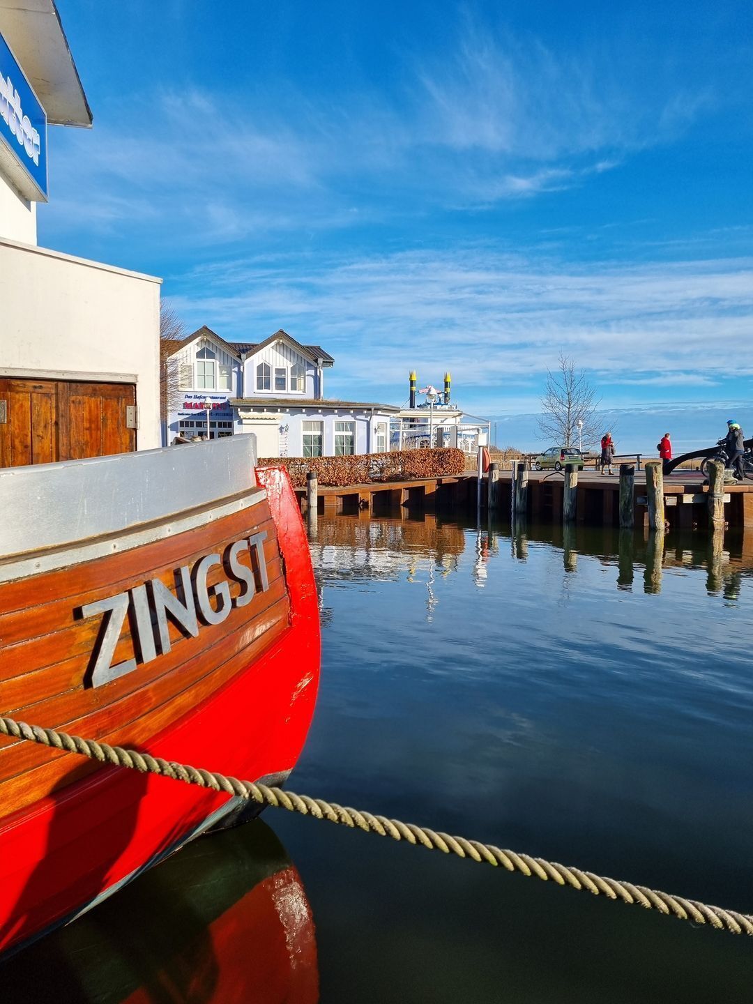 Ein rotes Boot namens ZINGSI liegt an einem Steg, im Hintergrund ein Gebäude.