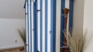 Ein Zimmer mit Holzboden, einem blauen und weißen Streifenkorpus und zwei hohen Vasen mit Trockenpflanzen.