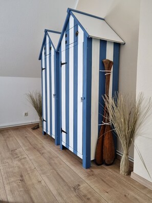 Une pièce dotée d’un plancher en bois, d’une armoire à rayures bleues et blanches, et de deux grands vases contenant des plantes séchées.