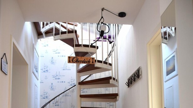 Eine Wendeltreppe mit einem Schild, auf dem 'Oberdeck' steht, die zu einem Raum mit gemustertem Wandpapier führt.
