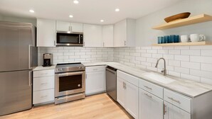 A modern kitchen with stainless steel appliances, white cabinetry, and a wooden shelf above the sink. - JHRL - Tensleep A11 - Minimalist, modern slopeside condo (Teton Village)