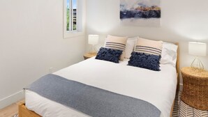 A bedroom with a large bed, two bedside tables, a window, and a painting on the wall. - JHRL - Tensleep A11 - Minimalist, modern slopeside condo (Teton Village)