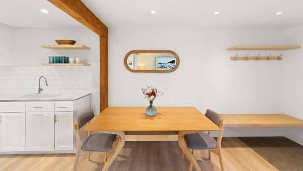 A modern kitchen with white cabinets, a wooden dining table, and a bench. - JHRL - Tensleep A11 - Minimalist, modern slopeside condo (Teton Village)