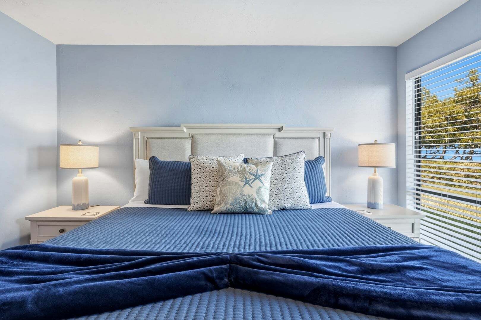 Une chambre à coucher avec un lit, deux tables de chevet et une fenêtre avec des stores.