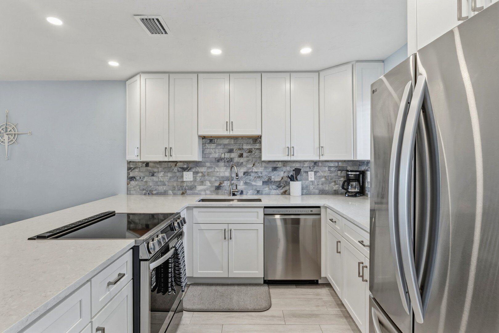 Una cocina moderna con armarios blancos, un refrigerador de acero inoxidable, horno empotrado y cafetera.
