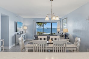 A dining area with a view of the sea, a chandelier, and a television on the wall.