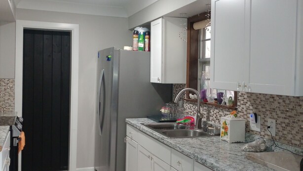 A modern kitchen with white cabinets, a stainless steel refrigerator, a granite countertop, and a tiled backsplash. - Nelly house (Oxford)