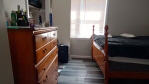 A bedroom with a wooden dresser, a bed, and a window with blinds. - Nelly house (Oxford)