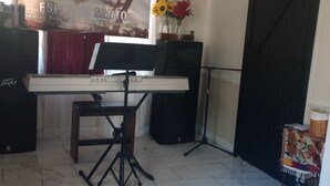 A room with a piano on a stand, a speaker, a banner on the wall, and a door. - Nelly house (Oxford)