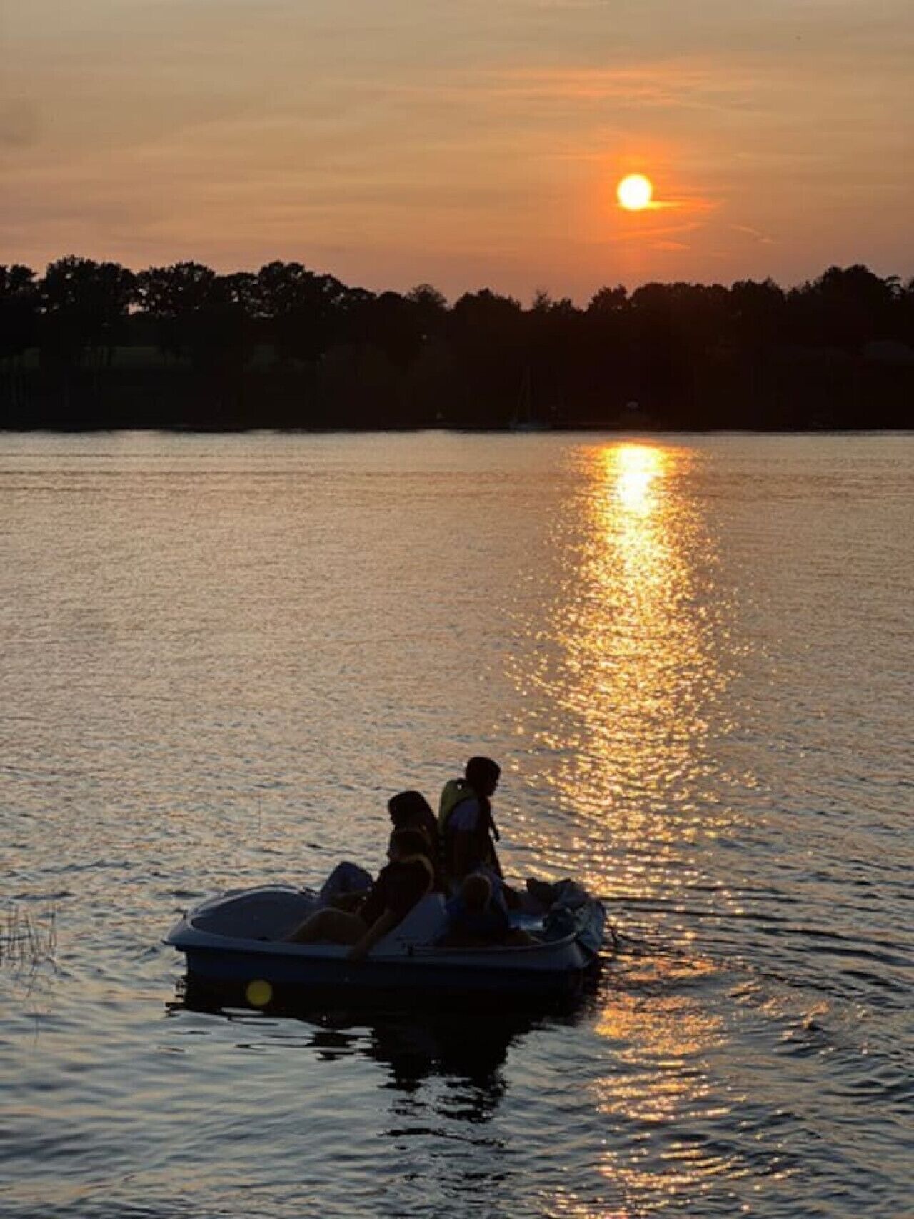 A sunset over a calm lake with a small boat carrying two people.