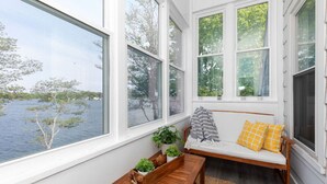Ein gemütliches Zimmer mit einer hölzernen Sitzbank, einer gepolsterten Sitzgelegenheit mit gelben Kissen und Blick auf einen See durch große Fenster.