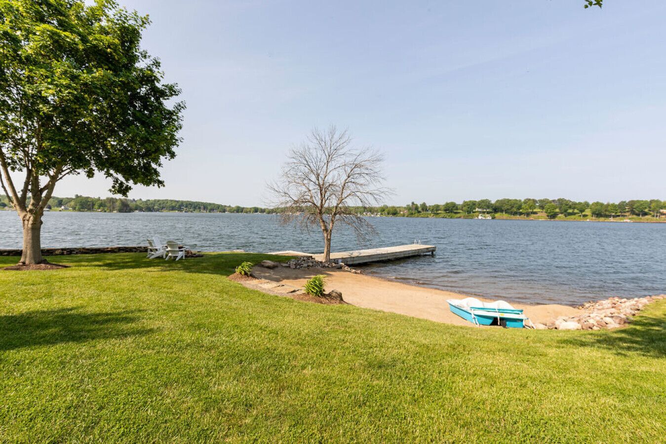 Une propriété au bord du lac, dotée d’un quai, d’un bateau et d’une zone herbeuse avec un arbre.