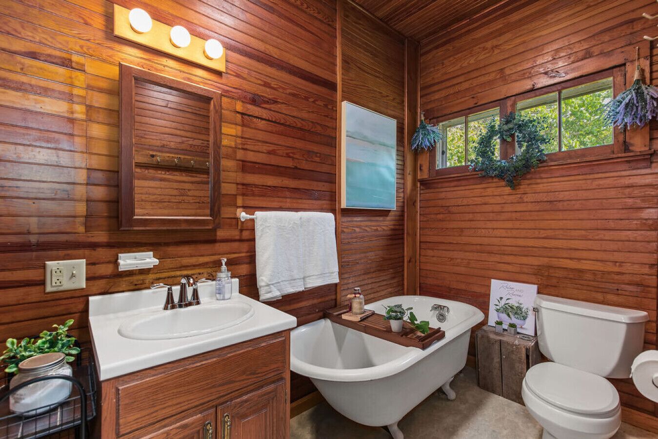 A wooden cabin bathroom with a white sink, clawfoot bathtub, and toilet.