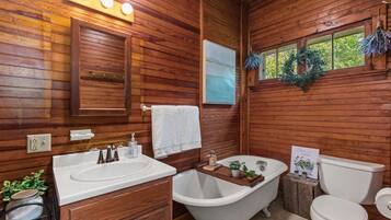 A wooden cabin bathroom with a white sink, clawfoot bathtub, and toilet.