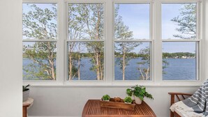 Ein Zimmer mit großem Fenster mit Seeblick, einem Holztisch mit Pflanzen und einer Bank mit gestreifter Decke.