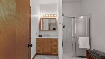 Une salle de bain avec un meuble-lavabo en bois, un miroir avec éclairage intégré, une douche et un banc avec des serviettes.