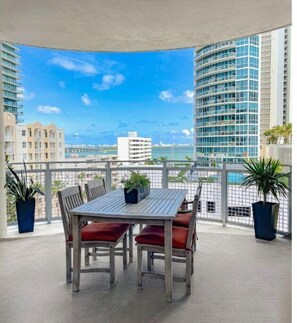 Enjoy a city view from this balcony with a table and chairs surrounded by lush plants.