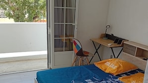 Ein Schlafzimmer mit Bett, Schreibtisch, Stuhl und einer Glasraumtür, die auf einen Balkon führt.
