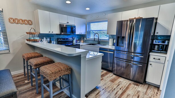 A modern kitchen with a central island, bar stools, stainless steel appliances, and a 'RELAX' sign on the wall. - Waterfront Sleeps 6 w/private boat dock and heated pool. (Crystal River)