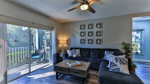 A spacious living room with a dark gray sofa, a wooden coffee table, and a ceiling fan. - Waterfront Sleeps 6 w/private boat dock and heated pool. (Crystal River)