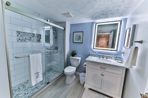 Ein Badezimmer mit Duschkabine aus Glas, einer weißen Toilette, einem Waschtisch mit Spiegel und einem gerahmten Bild an der Wand.