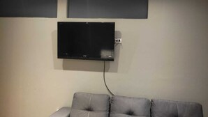 Un salon avec un téléviseur à écran plat fixé au mur, un canapé gris et une petite table.