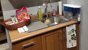 Une cuisine avec des meubles de rangement en bois, un four à micro-ondes, un évier avec un robinet et un panier de céréales sur le comptoir.