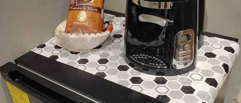 Eine Hamilton Beach BrewStation Kaffeemaschine zusammen mit einer Packung Folgers Kaffee auf einem Tisch mit sechseckigem Muster.