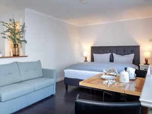 Une chambre d’hôtel moderne, équipée d’un lit, d’un canapé, d’une table à manger et d’un vase avec une plante.