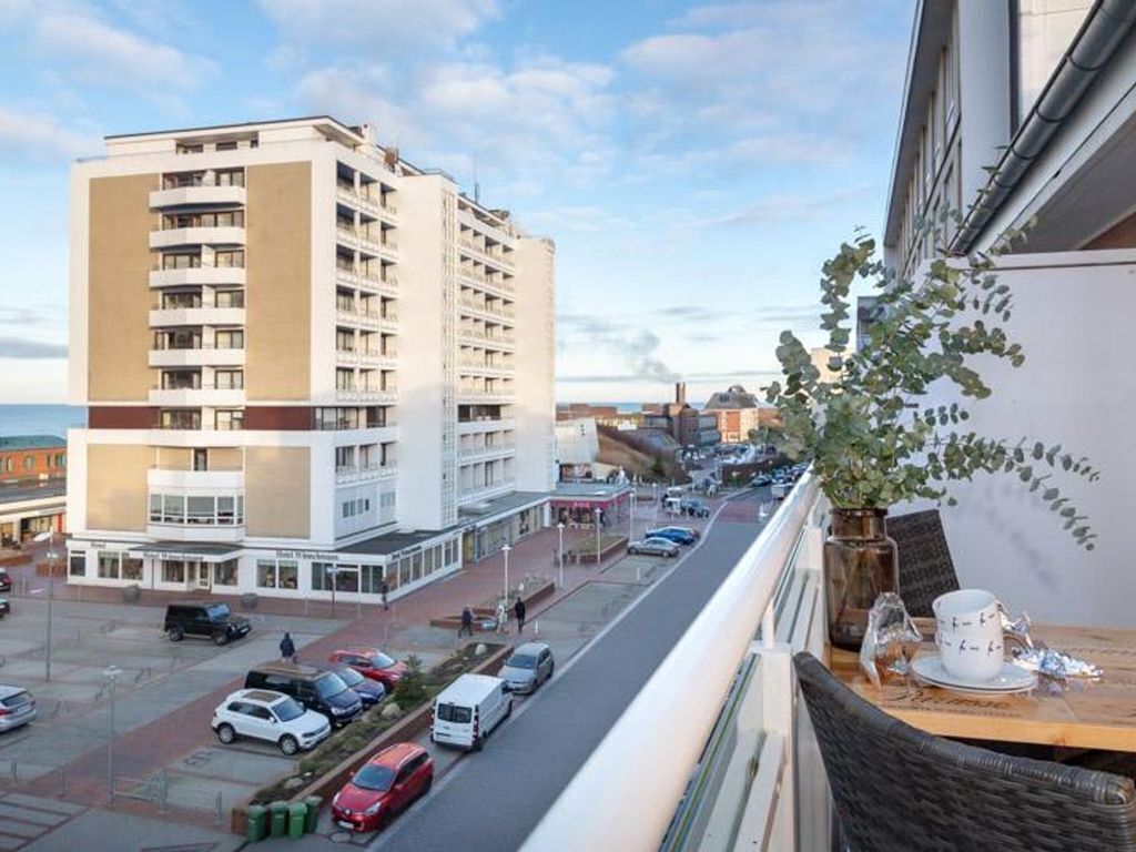 A hotel with a modern design, featuring a prominent white and beige facade, multiple balconies, and a view of the street and other buildings.