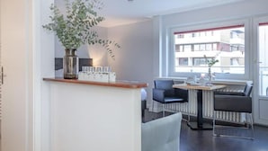 A modern kitchen with a central island, a dining area with a table and chairs, and a large window with a view of buildings. - Modern apartment with balcony, in direct beach location - Andreas-Dirks-Straße 5 (Sylt)
