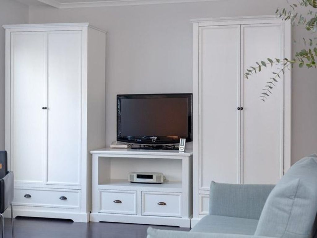 A living room with white cabinets, a flat-screen TV on a stand, a grey sofa, and a small table with a remote control.
