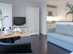 Un salon moderne doté d’un téléviseur à écran plat, d’une table à manger avec des chaises, d’un canapé bleu clair et d’un coin cuisine avec des placards et un four à micro-ondes.