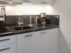 A modern kitchen with a stainless steel sink, a coffee maker, and a glass container. - 5th floor, ultra-modern one-room apartment with a balcony and a view. - Andreas-Dirks (Sylt)