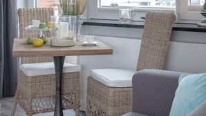 Ein gemütliches Zimmer mit Korbmöbeln, einem Tisch mit Früchten und einer Vase, und Blick durch ein Fenster.