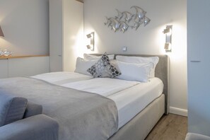 A neatly made bed with white linens and a grey throw blanket, a grey sofa, and a wall-mounted fish sculpture. - 5th floor, ultra-modern one-room apartment with a balcony and a view. - Andreas-Dirks (Sylt)