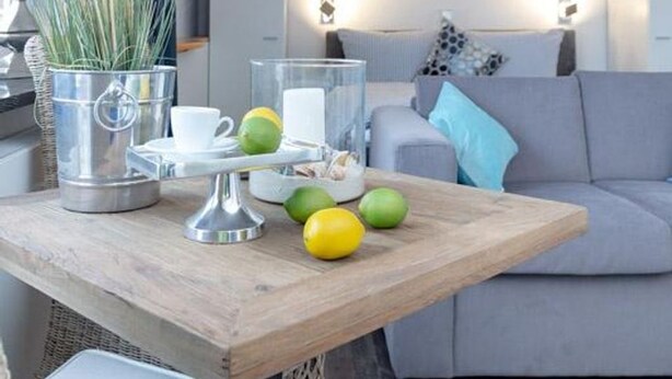 Ein Holztisch mit einer weißen Tasse, einem Glasbehälter und grünen und gelben Früchten.