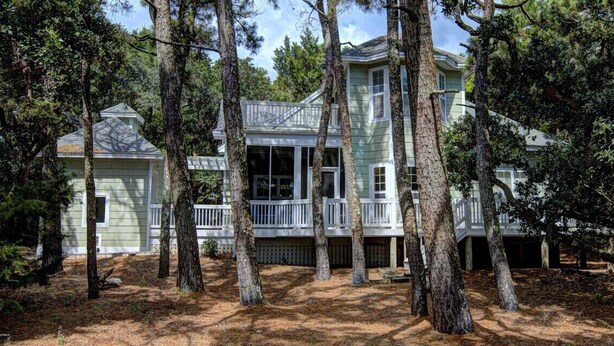 A two-story house with a balcony, surrounded by tall trees. - Ingen Trafikk secluded forest oasis (Bald Head Island)