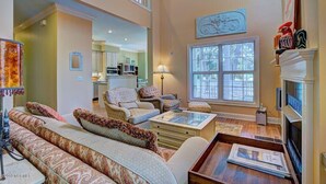 A spacious living room with a high ceiling, a fireplace, and a large window. - Ingen Trafikk secluded forest oasis (Bald Head Island)