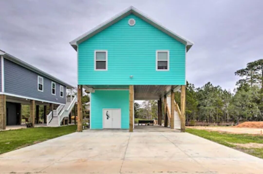 Une maison turquoise d’un seul étage, dotée d’un porche couvert, d’une porte d’entrée et d’un escalier menant à un deuxième étage.
