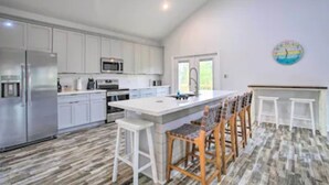 A modern kitchen with white cabinets, a stainless steel refrigerator, a microwave, and a large island with bar stools. - Bay St Louis Water Front Home w/ Private Pool + Boat Dock (Bay St Louis)