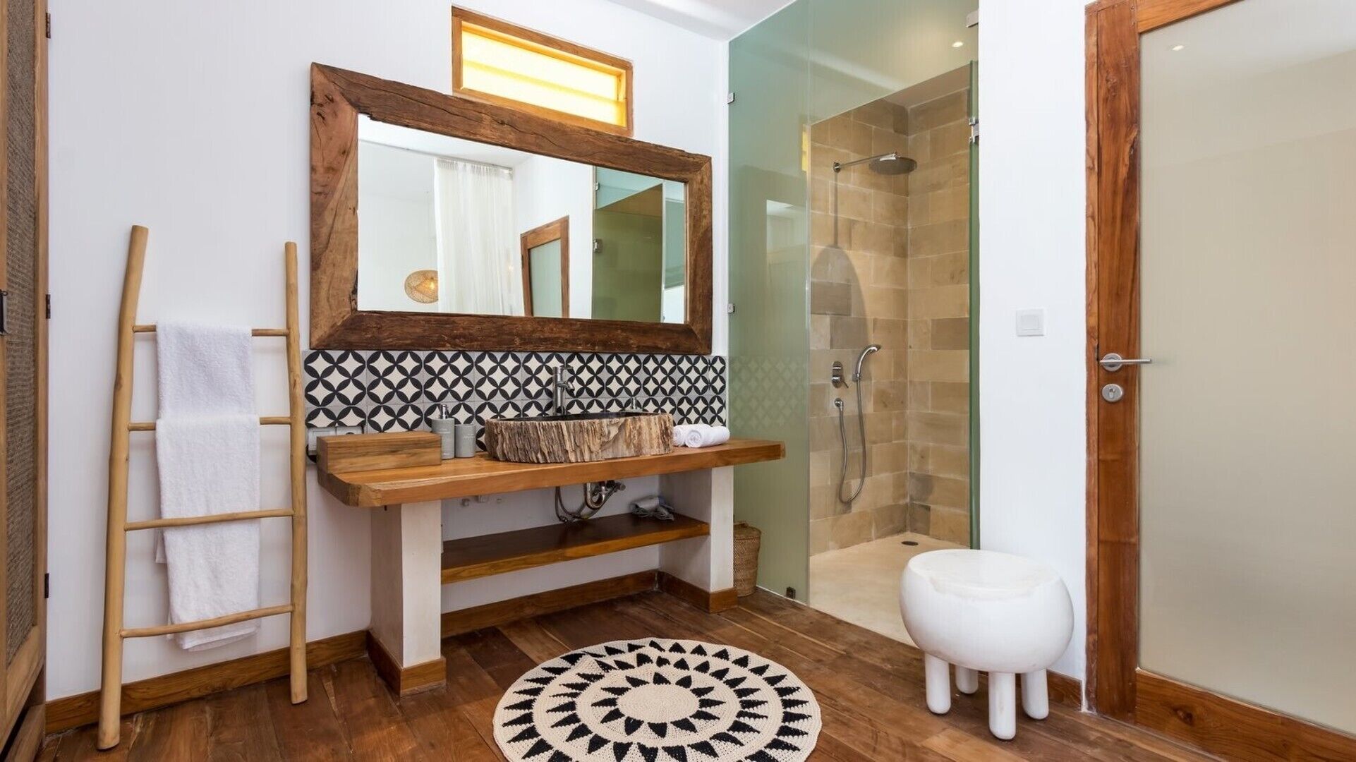 Un bagno con un mobile bagno in legno, un grande specchio, una doccia con porta in vetro e uno sgabello bianco.