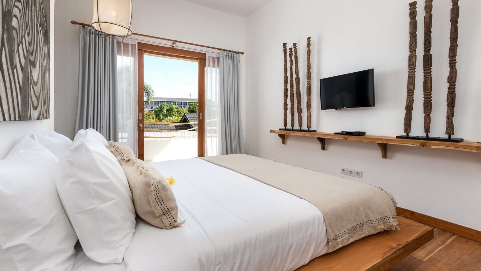 Une chambre à coucher avec un lit, un téléviseur fixé au mur et une fenêtre avec des rideaux.