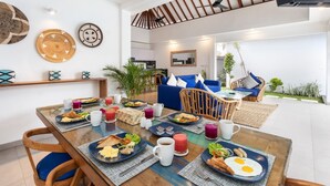 A dining area with a wooden table set for breakfast, including plates of eggs, toast, and fruit. There are wicker chairs and a blue sofa in the background. - Beautiful 3BR Villa W/ Private Pool in Bali, Bali Villa 2207 (Bali)