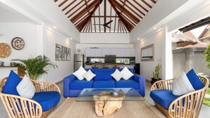 A modern living room with a blue sofa set, wooden chairs, a glass coffee table, and a ceiling fan. - Beautiful 3BR Villa W/ Private Pool in Bali, Bali Villa 2207 (Bali)