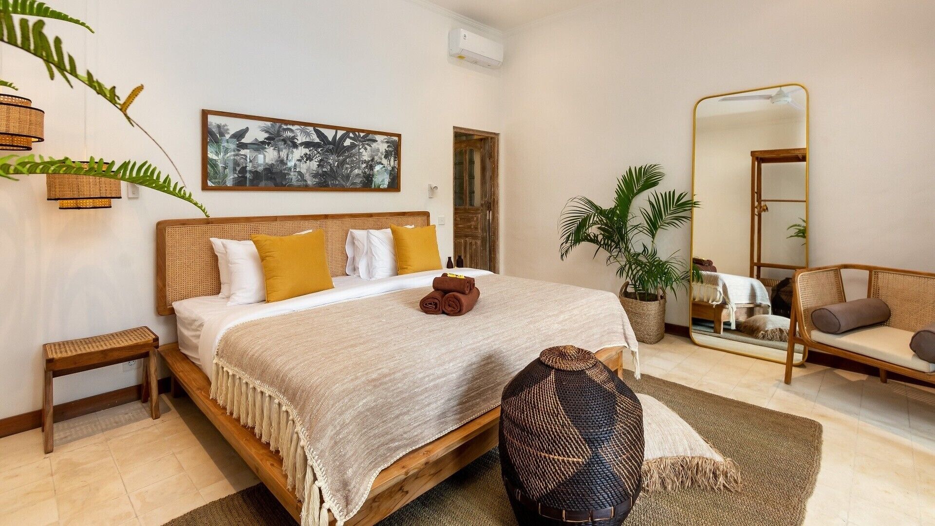 A well-lit bedroom with a bed, bedside tables, a mirror, a sofa, and a potted plant.