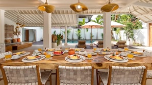 A spacious dining area with a long wooden table set for breakfast, surrounded by chairs, and overlooking a pool and lush greenery. - Wonderful 4BR Villa with Pool, Bali Villa 2212 (Bali)