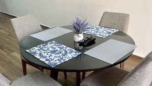 A round dining table with four grey upholstered chairs, a vase with purple flowers, and a remote control on the table. - Departamento con alberca en El Encanto (Mazatlán)